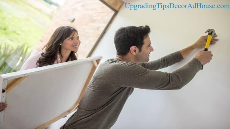 Couple decorating a wall with artwork using Decoration Tips DecorAdHouse From DecoratorAdvice to create a stylish living space.